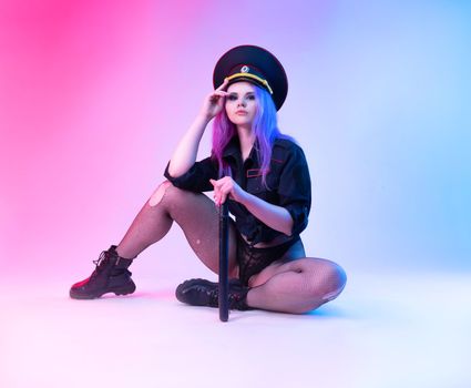Sexy girl in police military uniform posing in lingerie with a police rubber baton in neon light