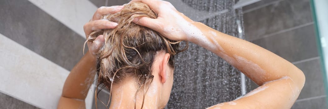 Young woman washes her hair with shampoo and hands with foam closeup