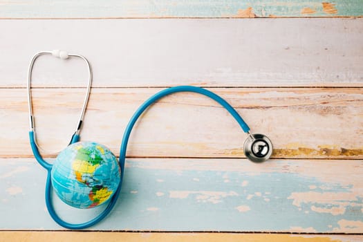 World Health Day. Blue doctor stethoscope and world globe isolated on wood background with copy space, Save world day, Green Earth, Healthcare and medical concept