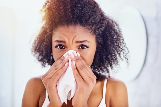Oh no, could it be flu. an attractive young woman blowing her nose with a tissue at home.