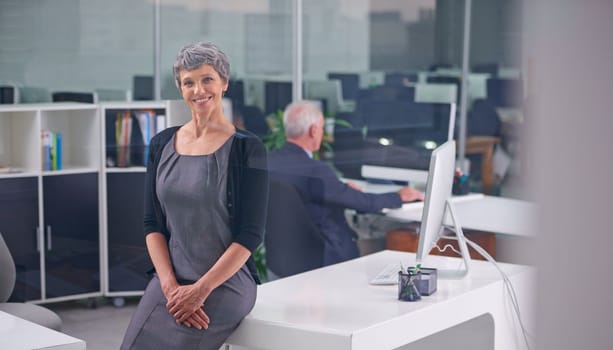 Successful and satisfied in her job. A smiling mature businesswoman at her desk with a coworker in the background.