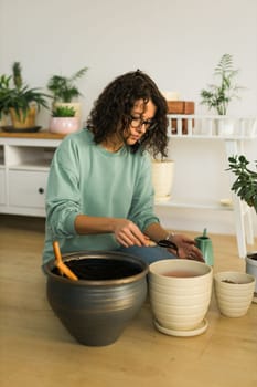 Woman gardener transplanting green plants in ceramic pots on the floor. Concept of home garden and potted plants