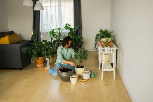 Spring hobby happy young woman transplanting in flower pot houseplant with dirt or soil at home. Gardening plant and green tropical concept