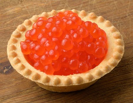 Red caviar in a round tartlet on a wooden background