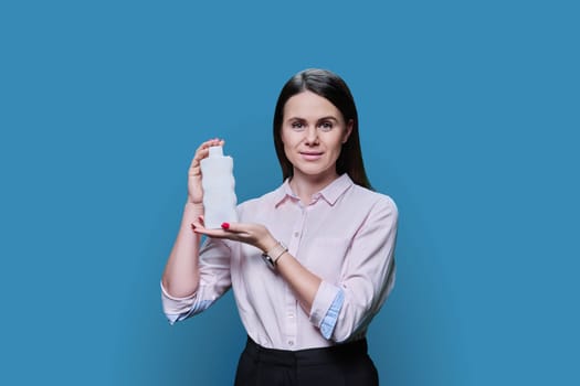 Young woman holding empty tube with shampoo balm mask on blue background