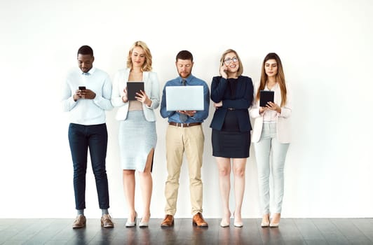 Concentrating is part of what they do. a group of work colleagues standing in a line while using their wireless devices against a white background.