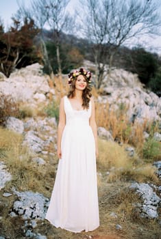 Smiling bride in a multi-colored wreath stands on a mountain among the stones