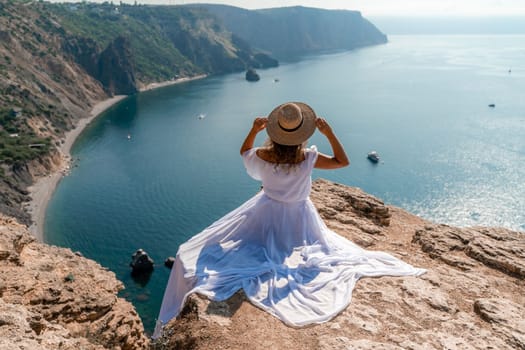 Woman sea. A happy girl is sitting with her back to the viewer in a white dress on top of a mountain against the background of the ocean and rocks in the sea.