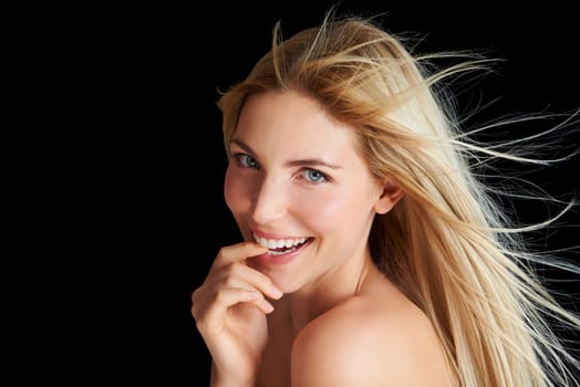 Soft and silky hair. A blonde woman posing in front of a black background while the wind blows through her hair.