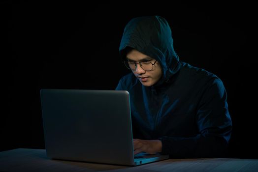 Asian hacker hacking computer network with laptop in dark. Cyber security concept