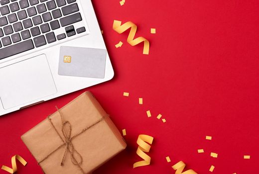 Shopping online with credit card for christmas holiday. Laptop with gifts on table on red background