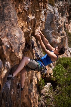 This makes her feel alive. a young woman gripping a ledge while rock climbing.