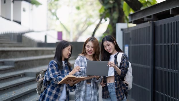 Nice young students use laptop after class sitting outdoors. girls wear casual clothes in spring. Concept of modern education