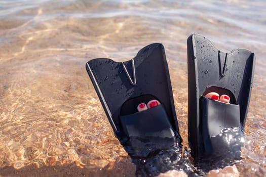 A woman in black flippers splashes near the shore. Fins stick out 