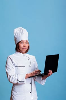 Smiling chef with apron holding laptop computer checking culinary recipe ingredient list