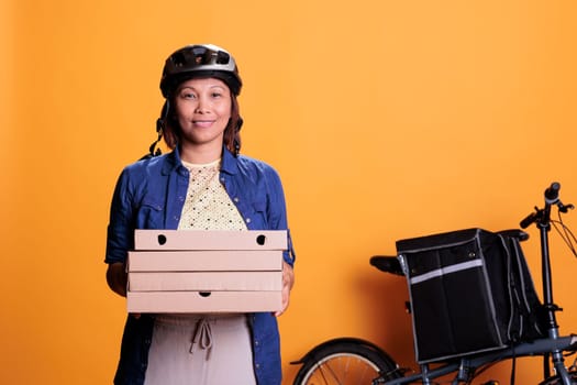 Portrait of deliverywoman wearing helmet and pizzeria uniform carrying pizza cardboxes