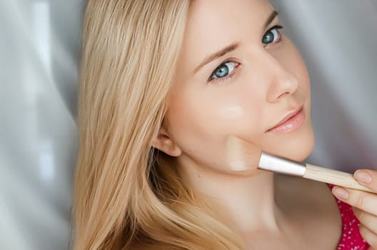 Beautiful blonde woman applying liquid make-up foundation on her skin with make-up brush