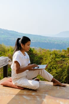 Young Asian woman digital nomad traveler working online on laptop in the mountains