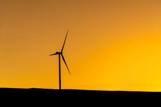 Wind turbine standing on a hill at sunset and generating electricity