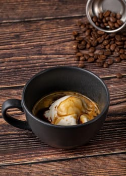 Espresso with ice cream in black porcelain cup on wooden table. Affogato Coffee