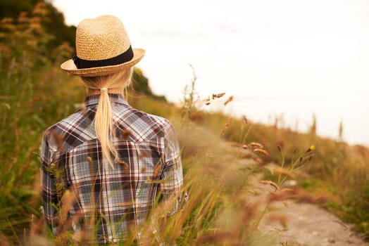 Chase your dreams but always know your way back. Rearview of a woman in a field wearing a straw fedora.