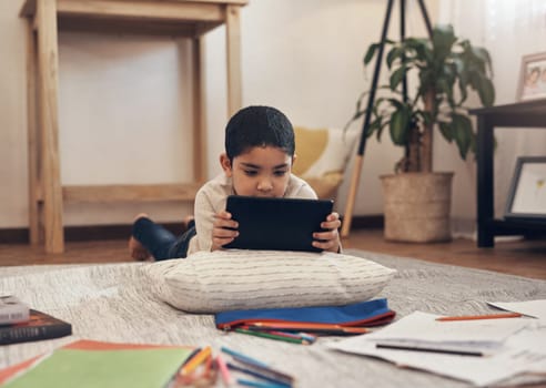 One smart app for one smart kid. an adorable little boy using a digital tablet and headphones while completing a school assignment at home.