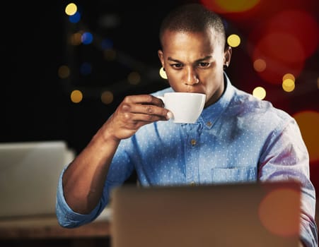 Some caffeine to keep him going. a young man drinking an espresso while working late night on his laptop.