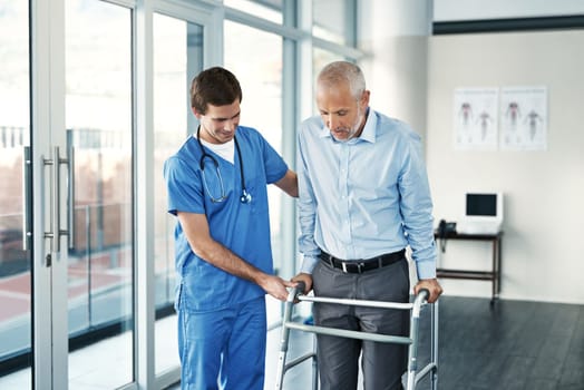 Slow and steady steps. a male nurse assisting a senior patient with a walker.