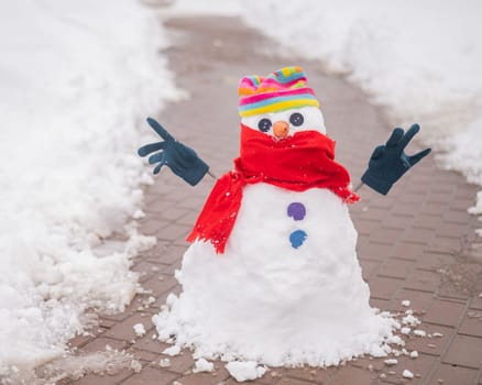 Snowman in a hat and gloves on the sidewalk from paving slabs.