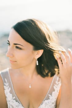 Bride in a white dress straightens her hair in the wind with her hand. Portrait