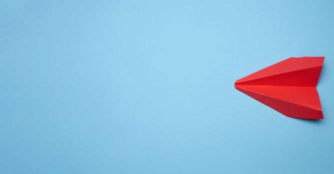 Red paper airplane on a blue background, travel concept, top view. Copy space