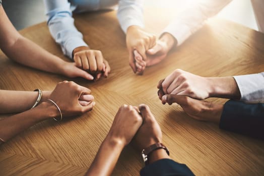 We are nothing without each others strength and support. Closeup shot of a group of businesspeople sitting together at a table and holding hands.