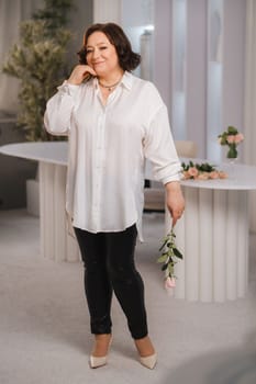 An adult woman in a white shirt holds one rose in her hands while standing in the interior. Pink roses