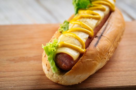 Cheese hot dog with mustard on the wooden board