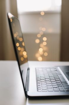 Close up of laptop keyboard with blank screen on a table by blurry bokeh lights background in the house or office modern, sunlight in morning