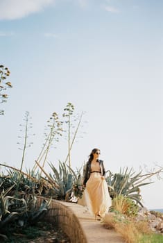 Bride in sunglasses walks along a stone curb past agave bushes