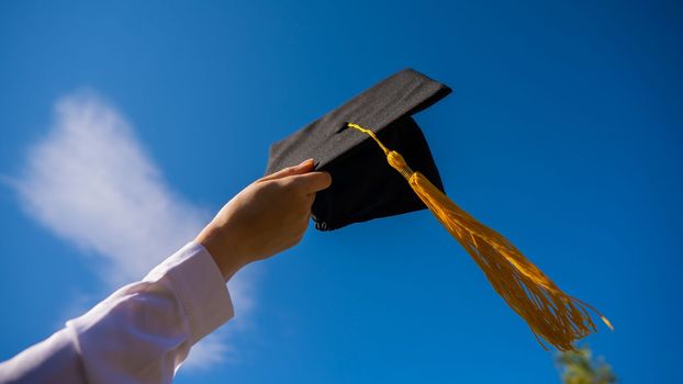 Close-up of a woman's hand with a graduation cap against the blue sky.