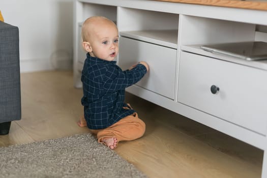 Toddler baby boy open cabinet drawer with his hand. Child explore what is in cabinet. Baby curiosity and child development stages