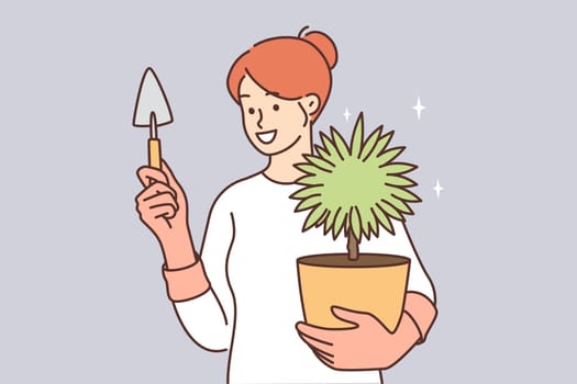Woman caring for house plant in pot holds shovel to replace earth or transplant flower