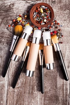 Cosmetics products and brushes in conceptual image over wooden background