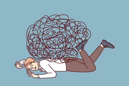 Depressed businessman lies on ground face down under heavy load of tangled lines