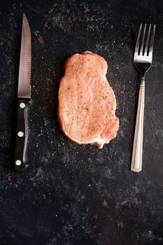 Raw steak meat on black wooden table next to fork and knife