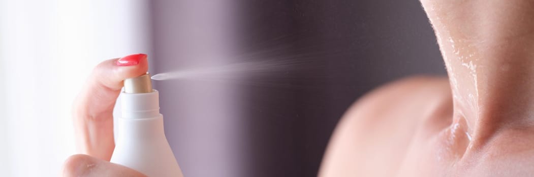 Woman spraying perfume or moisturizing skin lotion on neck closeup