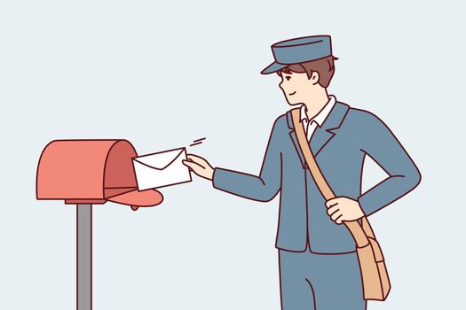 Man in postman uniform throws paper letter into metal mailbox located on street