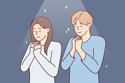 Young coupl man and woman stand with eyes closed praying asking god for happy marriage