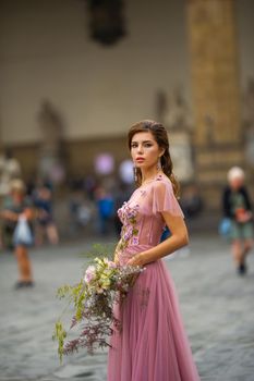A bride in a pink dress with a bouquet stands in the center of the Old City of Florence in Italy