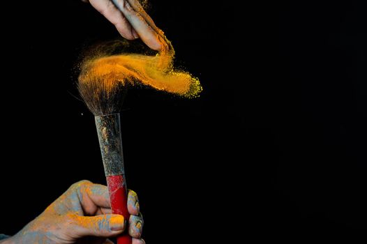 Woman shaking off orange powder from a brush on a black background.