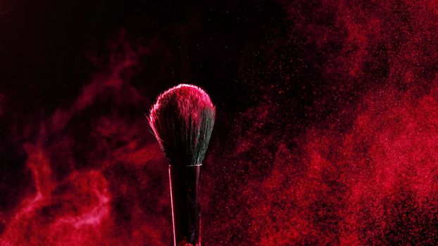 Makeup brush with an explosion of red powder on a black background.