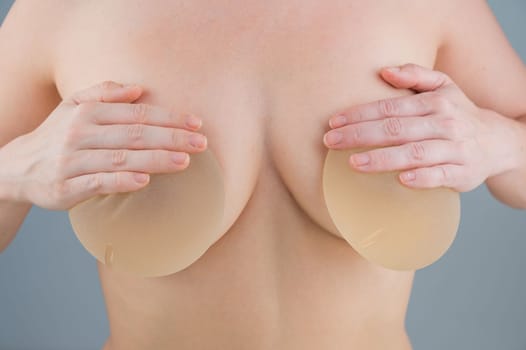 Caucasian naked woman trying on silicone breast implants.