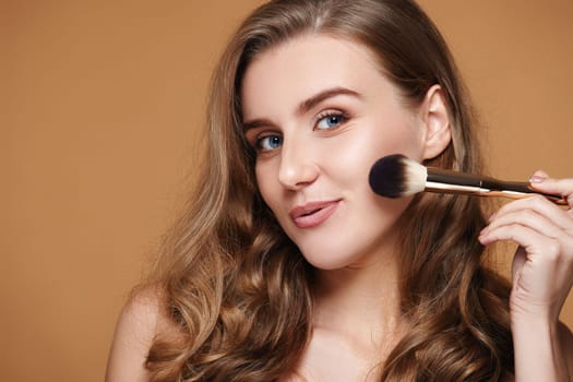 smiling woman applying blush on cheeks with make-up brush